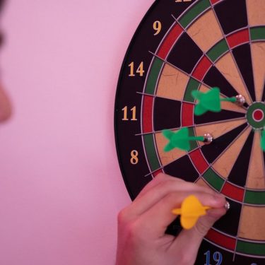 A person focusing on adjusting darts on a dartboard, symbolizing precision and leisure.