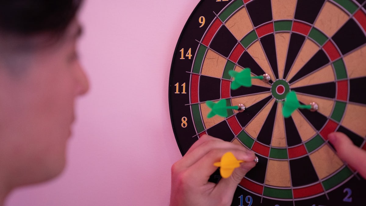 A person focusing on adjusting darts on a dartboard, symbolizing precision and leisure.